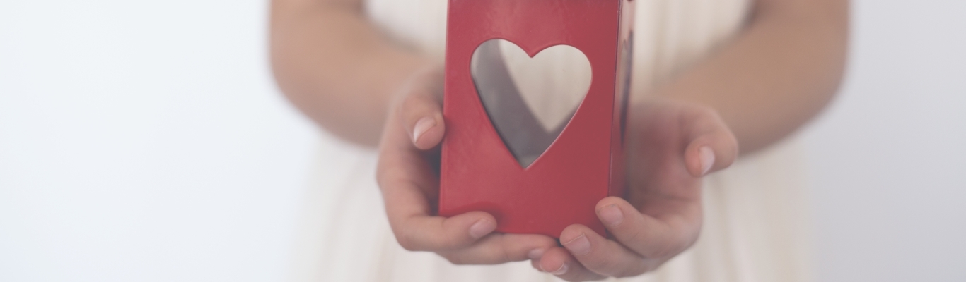 Child's hands holding a red metal lantern with a heart shaped cut out
